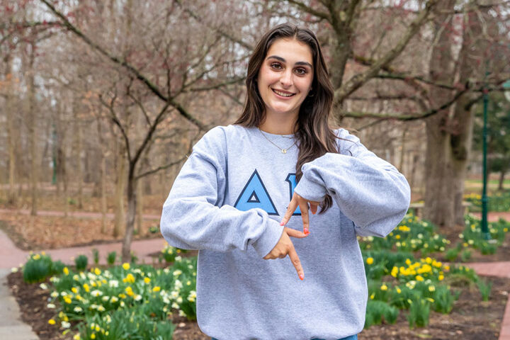 Female wearing a Delta Gamma sweatshirt poses on campus on a spring day.